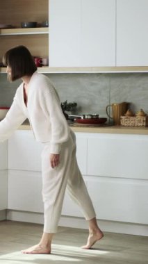 Yoğunlaşmış Kafkasyalı orta yaşlı kadın ev işleriyle meşgul ve evdeki mutfakta yerleri süpürüyor. Ev işi ve temizlik kavramı. Dikey video.