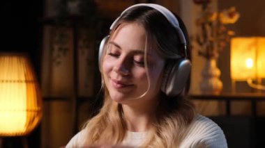 Kablosuz kulaklık takan, müzik dinleyen ve hafta sonu evde dinlenen beyaz bir kadın..
