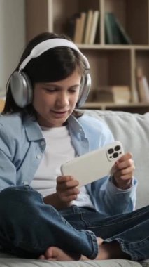 İnternetteki video oyununda telefonla oynayan ve evdeki mağlubiyet ya da mağlubiyetten rahatsız olan beyaz bir çocuk. Dikey video.