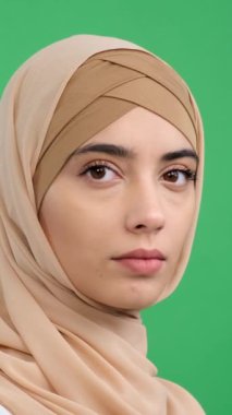 Yeşil arka plandaki kameraya bakan tesettürlü, mutlu ve gülümseyen Arap bir kadının portresi. İnsanların bireysellik kavramı. Dikey video.