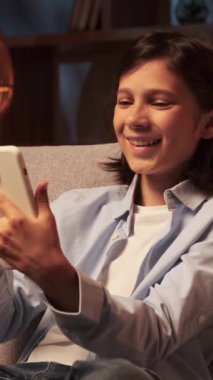 Mutlu ve neşeli Kafkasyalı genç çocuk internette mesajlaşıyor ve gece geç saatlerde cep telefonuyla internette geziniyor. Dikey video.