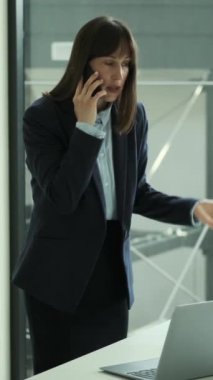 Ofiste çalışan, telefonla konuşan orta yaşlı, ciddi bir beyaz kadın. Konuşma, müzakere, iletişim kavramı. Dikey video.