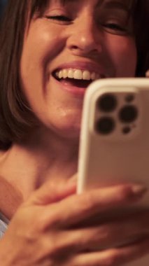 İnternette telefonla eğlenen ve evde gülen mutlu beyaz bir kadının portresini yakından çek. Dikey video.