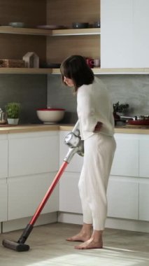 Evdeki mutfak zeminini süpüren sıkıcı ya da yorgun orta yaşlı beyaz kadın. Ev işleri ve günlük ev işleri. Dikey video.