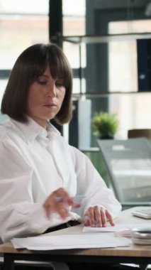Düşünceli Kafkasyalı kadın ofis çalışanı mali belgeleri gözden geçiriyor, ofiste başlangıç stratejisi ve muhasebe işi geliştiriyor. Dikey video.