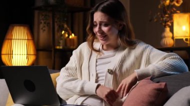 İnternette film ya da internet şovu izleyen, gülen ve akşam evinde dizüstü bilgisayarla kanepede dinlenen olumlu beyaz kadın..
