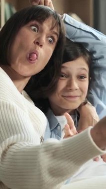 Oyuncu beyaz anne ve oğlu evde online sosyal medya için telefon kullanıyor ve selfie çekiyor. Boş zamanlarımızı birlikte geçiriyoruz. Dikey video.