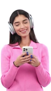 Beyaz arka planda akıllı telefon kullanarak internette gezinen ve müzik dinleyen gülen beyaz bir yetişkin kadın. Dikey video.