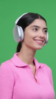 Yeşil arka planda kulaklıkla müzik dinleyen mutlu beyaz bir kadının profil portresi. Zevk ve memnuniyet kavramı. Dikey video.