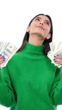 Finansal zenginliği kutlayan neşeli, genç, beyaz arka planda duran, para yığınları tutan beyaz bir kadın. Dikey video.