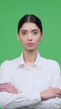 Yeşil arka planda, konsantre ve resmi olarak genç, beyaz bir kadının portresi. Güvenilir ve ciddi bir insan kavramı. Dikey video.