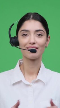 Kafkasyalı mutlu bir yardımcı ajanın portresi yeşil arka planda müşteriyle konuşurken kulaklık takıyor. Dikey video.