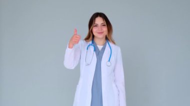 Kafkasyalı genç, yetişkin bir doktor ya da hemşire. Başparmak göstermesi ya da onaylama ve gri arka planda doğrulama gibi hareketler..
