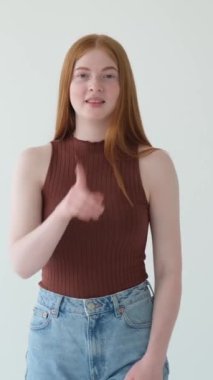 Beyaz arka planda duran mutlu kızıl saçlı beyaz kız, sessiz ol jesti yapıyor. Dedikodu ya da sır tutmak. Dikey video.