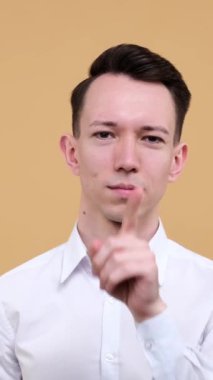 Heyecanlı genç, beyaz bir adam bej arka plan hakkında gizli bilgi saklama konusunda sessiz bir jest yapıyor. Gizlilik ve gizlilik kavramı. Dikey video.
