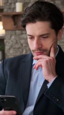 Konsantre beyaz erkek ofis çalışanı boş zamanlarını online sosyal medya cep telefonuyla geçiriyor, evdeki koltukta dinleniyor. Dikey video.