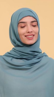 Gülümseyen Arap genç yetişkin kadın video kaydedicisi internet sosyal medyası için video kaydediyor ve bej arka planda izleyicilerle sohbet ediyor. Dikey video.