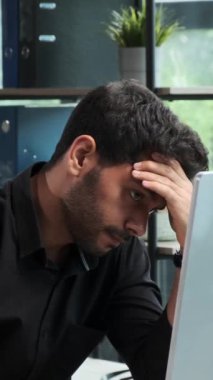 Memnun olmayan genç Orta Doğulu ofis çalışanı ofiste çalışırken sinir krizi geçiriyor ve baş ağrısı çekiyor. Aşırı yükleme ve iflas kavramı. Dikey video.