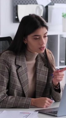 Ciddi bir beyaz kadın ofis çalışanı. İnternetten iş arkadaşlarını azarlıyor. Laptop kullanıyor, ofiste çalışıyor. Dikey video.