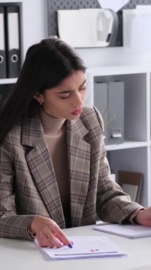 Sert kadın, Kafkasyalı, genç, serbest çalışan, ofiste evrak işleriyle uğraşan biri. Finansal belgeleri inceler ve incelerler. Dikey video.
