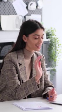 Ofiste video görüşmesi ve evrak işleriyle uğraşan beyaz kadın bir ofis çalışanı var. Müşteri ile iletişim kurma kavramı. Dikey video.