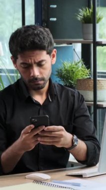 Ofiste çalışırken telefonu kullanan ve zaferi ya da iyi haberi kutlayan Ortadoğulu erkek serbest yazar hayrete düştü. Dikey video.