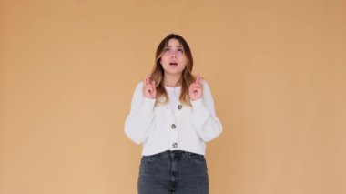 Kendinden emin ve konsantre beyaz kadın umut içinde dua ediyor bej arka planda dua ediyor. Şans, arzu, dilek jesti.