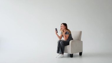 Beyaz arka planda telefon ile çevrimiçi sosyal medya için video kaydeden genç beyaz kadın blogcu. Canlı yayın..