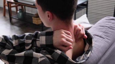 Evdeki oturma odasında ağrı kesici için boyun masajı yapan sağlıksız ve sağlıksız beyaz bir gencin arka görünüşü. Kramp veya travma kavramı.