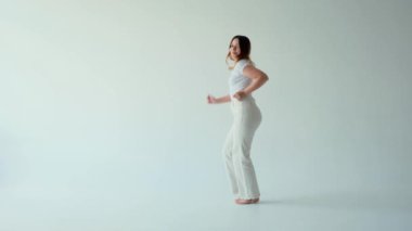 Dinamik, mutlu ve iyimser beyaz arka planda neşeli bir şekilde dans eden beyaz bir kadın. Etkin eğlence konsepti.