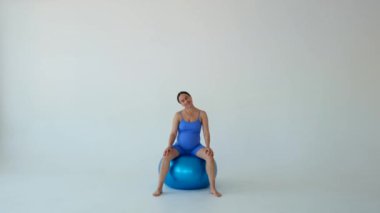 Gülümseyen ve pozitif hamile orta yaşlı beyaz kadın spordan önce ısınıyor, spor yapıyor, beyaz arka planda oturuyor..