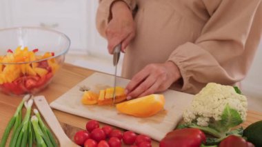 Orta yaşlı hamile bir kadının mutfakta domates ve sebzeli salata pişirirken yakın plan fotoğrafı. Hamilelik ve sağlıklı gıda kavramı.