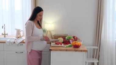 Neşeli beyaz orta yaşlı hamile kadın ev mutfağında salata için sebze hazırlıyor. Günlük mutfak işleri kavramı..