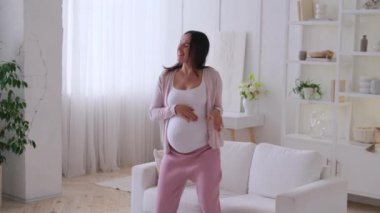 Neşeli hamile, orta yaşlı, beyaz bir kadın boş zamanlarını evde dans ederek ve eğlenerek geçiriyor. Mutlu çocuk beklentisi kavramı.