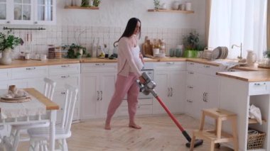 Mutlu orta yaşlı beyaz hamile kadın evini temizliyor ve yerleri süpürüyor. Hamilelik süresince ev işleri ve ev temizliği kavramı.