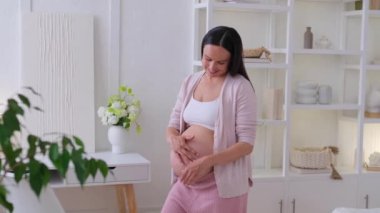 Mutlu beyaz orta yaşlı kadın, evinde hamile bir karnı sıcacık okşuyor. Hamilelik, beklenti ve çocuk sevgisi kavramı.