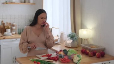 Mutlu orta yaşlı, beyaz hamile kadın salata için sebze kesiyor ve mutfakta dans ediyor. Günlük yemek rutini kavramı.