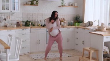 Gülümseyen orta yaşlı hamile bir kadın evde eğleniyor ve dans ediyor, hamileliği ve gelecekteki anneliği kutluyor..