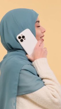 Neşeli Arap genç yetişkin kadın telefonla konuşuyor, bej arka planda duruyor. Uzaktan sohbet ve bağlantı kavramı. Dikey video.