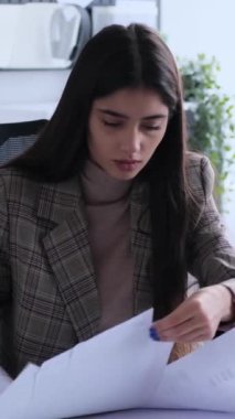 Ofiste evraklarla çalışan, hayal kırıklığına uğramış, genç, beyaz bir kadın çalışan. Sorun kavramı, kaos ve gerilim. Dikey video.