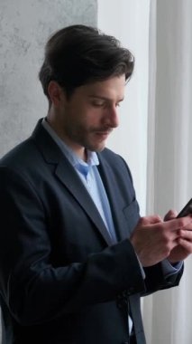 Düşünceli, genç, yetişkin, Kafkasyalı, ofisteki akıllı telefonu kullanarak internetten mesajlaşıyor. Siber uzayda iletişim kavramı. Dikey video.