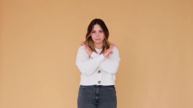 Ciddi ve sert beyaz kadın bej arka planda dur işaretinde kollarını kavuşturuyor. Yasak, protesto ve koruma kavramı.