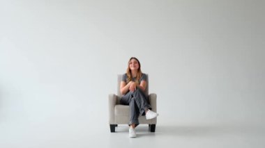 Kafkasyalı mutlu ve büyüleyici genç bir kadının portresi koltukta dinleniyor ve beyaz arka planda kameraya bakıyor. Kadın kadınlık kavramı.