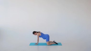 Hamilelik eğitimi sırasında beyaz arka planda yoga yapan orta yaşlı, beyaz, hamile bir kadın. Dinlenme ve rahatlama kavramı.