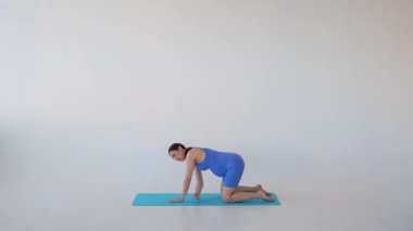 Pozitif hamile, orta yaşlı, beyaz arka planda beden eğitimi ya da yoga eğitimi alan beyaz bir kadın..