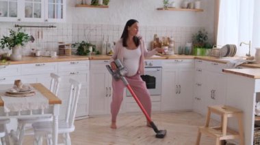 Pozitif hamile, orta yaşlı, beyaz kadın dans ediyor ve ev mutfağını süpürüyor. Ev işi ve yer temizliği kavramı.
