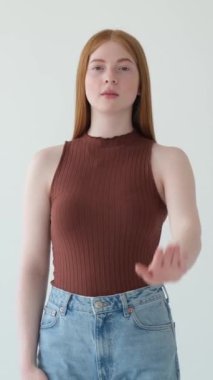 Beyaz arka planda avuçlarında yasak, savunma ya da koruma işareti olan ciddi bir beyaz kız. Dikey video.
