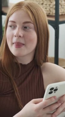 Kafkasyalı mutlu bir kız cep telefonunu internet ve internet eğlencesine mesaj atmak için kullanıyor, boş zamanlarını evde geçiriyor. Dikey video.