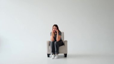 Beyaz arka planda yumuşak koltukta oturan, telefonla konuşan beyaz, genç, beyaz bir kadını gücendirdim. Uzaktan tartışma, sohbet veya diyalog.