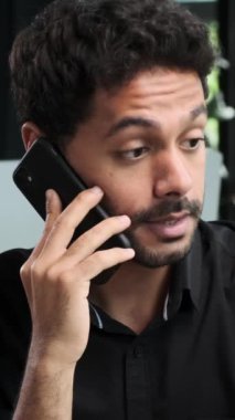 Ofiste çalışırken arkadaş canlısı Orta Doğulu serbest çalışan bir adam telefonla konuşuyor. Uzaktan konuşma ya da müzakere kavramı. Dikey video.